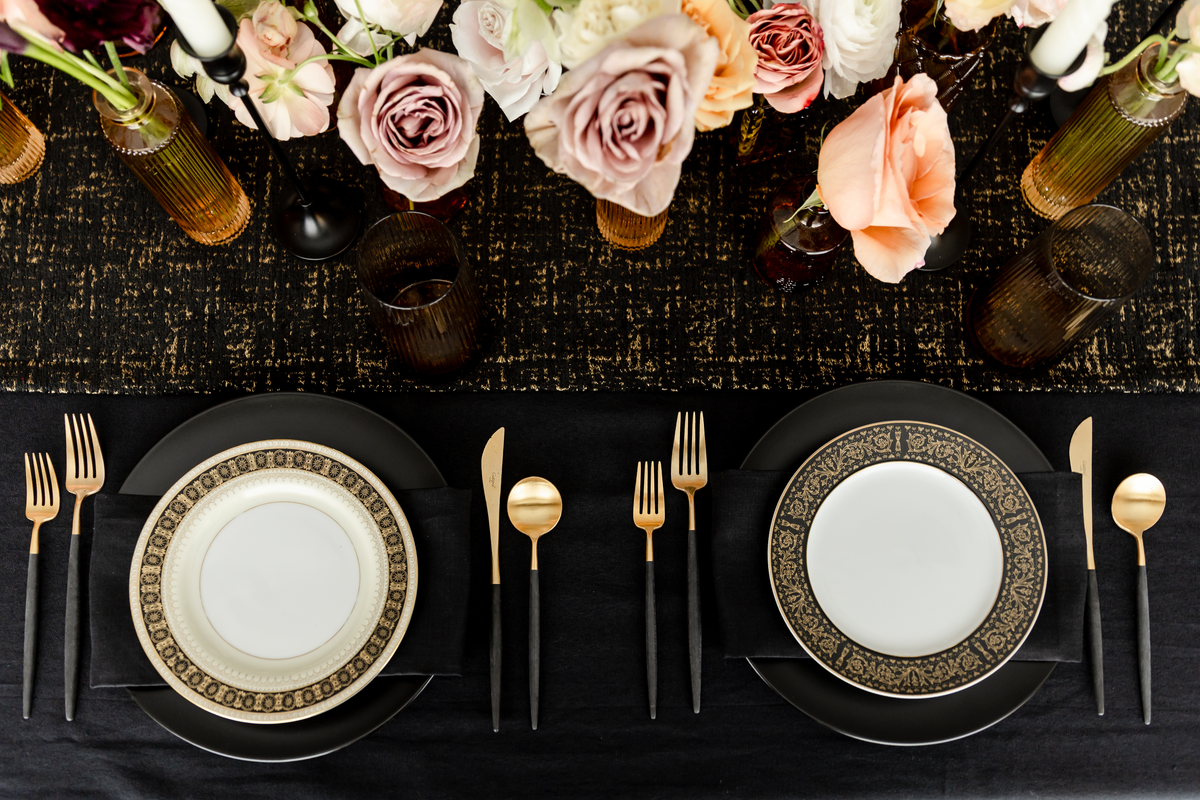 Elegant black and gold table setting with black dinner plates, vintage gold and black rimmed plates, amber glassware and floral arrangements.
