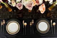 Elegant black and gold table setting with black dinner plates, vintage gold and black rimmed plates, amber glassware and floral arrangements.