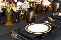 Elegant black and gold table setting with black dinner plates, vintage gold and black rimmed plates, amber glassware and floral arrangements.