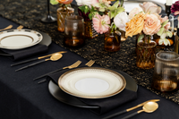 Elegant black and gold table setting with black dinner plates, vintage gold and black rimmed plates, amber glassware and floral arrangements.