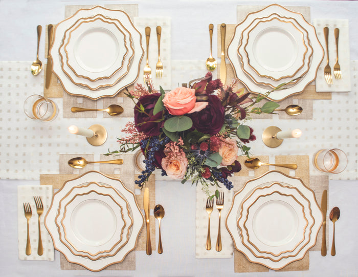 A table setting with gold and cream colored tableware including plates, glasses, and gold flatware for rent, gold rim dinnerware for rent, gold and ivory tablescape for rent